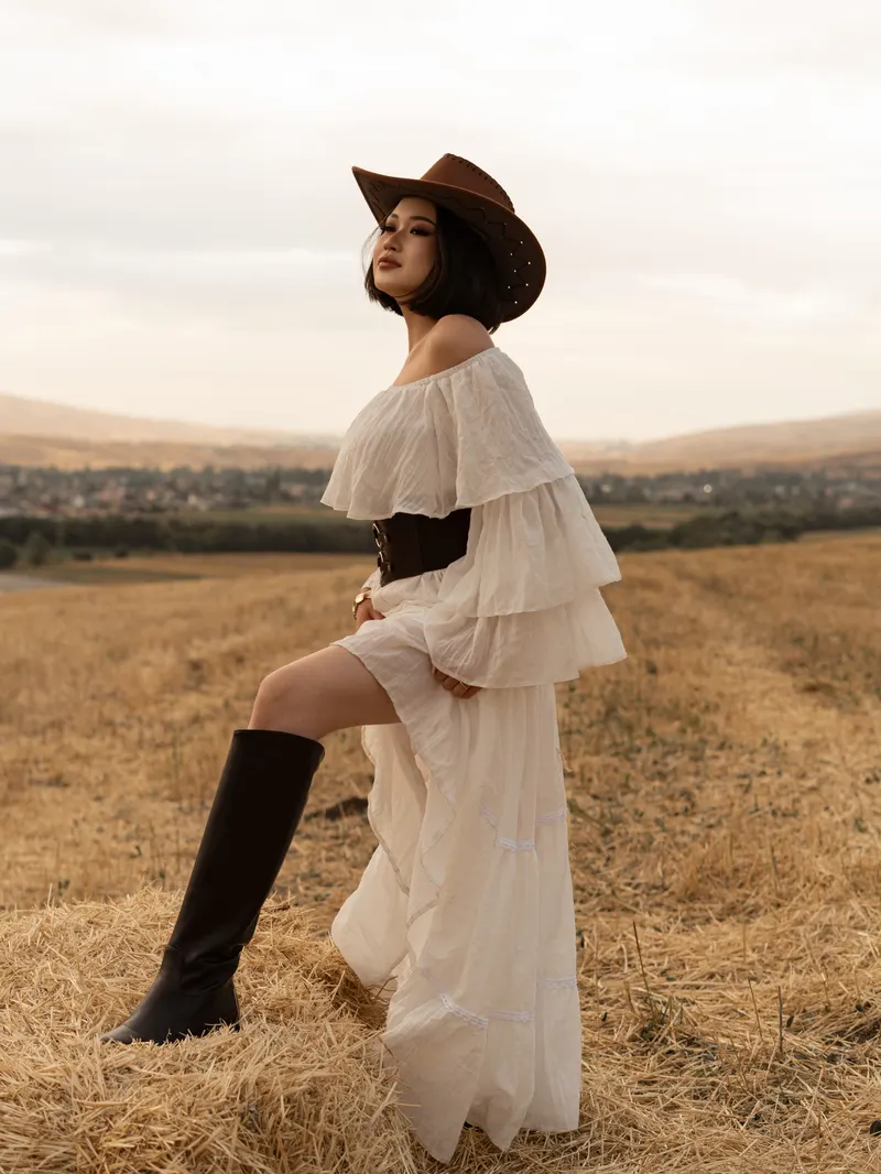 A woman in a white dress and cowboy hat on a straw bale